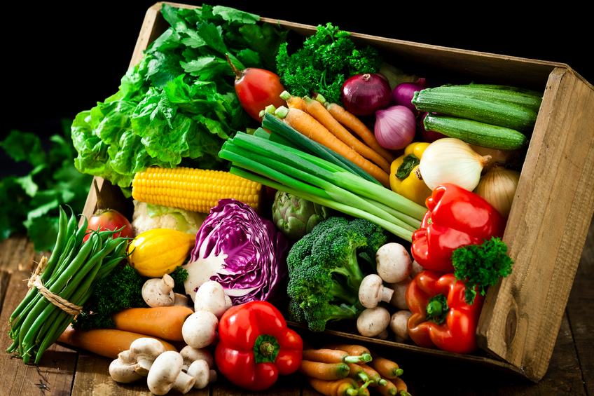 A wooden crate is filled with fresh, colorful organic vegetables. The crate is tilted and some vegetables are out of it on a rustic wood table. DSRL studio photo taken with Canon EOS 5D Mk II and Canon EF 70-200mm f/2.8L IS II USM Telephoto Zoom Lens