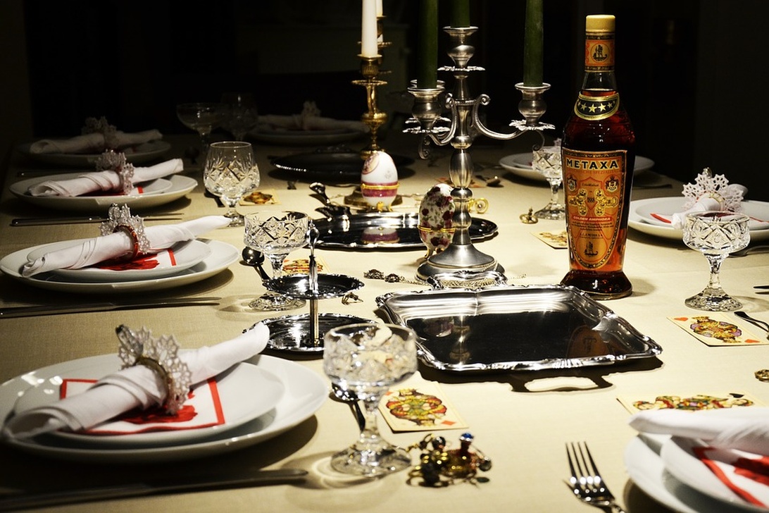 En formell dukning med vit bordsduk, kristallglas, silverkandelabrar och eleganta kuvert. Bordet har dekorativa servetter och silverfat.